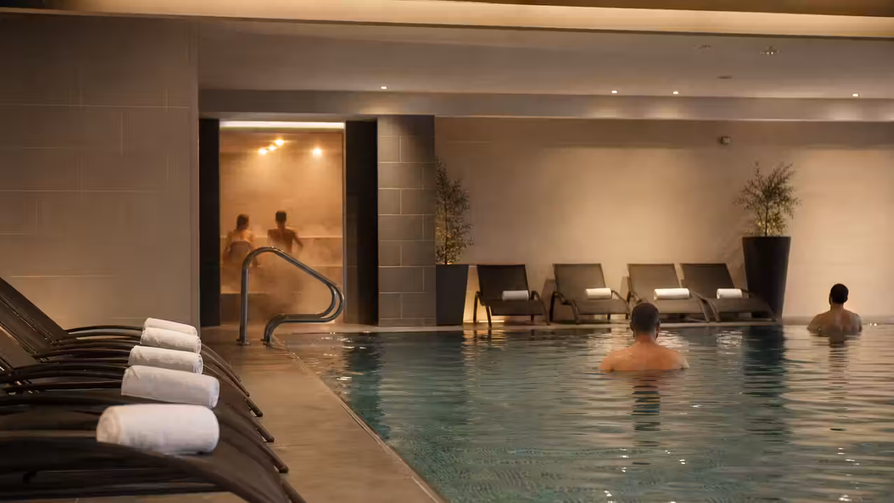 Espace bien-être d’une piscine publique avec bassin chaud, vapeur discrète et lumière tamisée en soirée