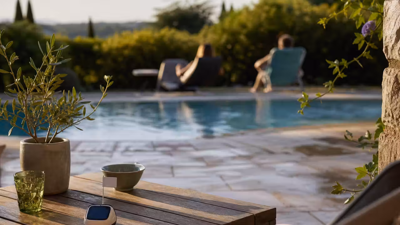 Signal connecté avec petit fanion installé sur une terrasse, à distance d’une piscine familiale en été