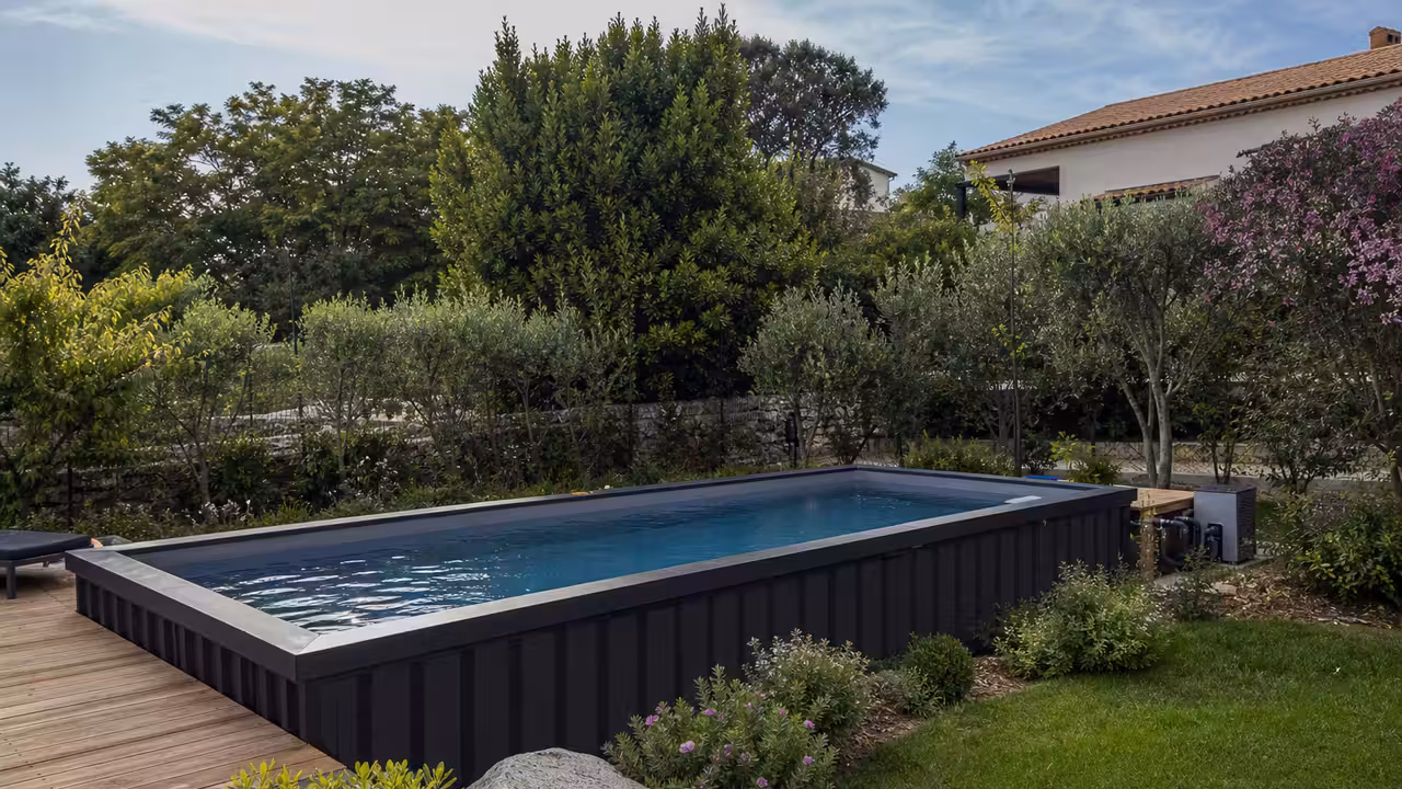 Piscine container anthracite installée sur une terrasse en bois dans un jardin contemporain et arboré