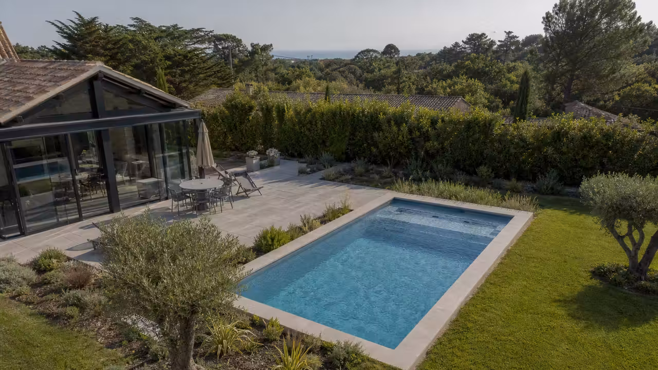 Piscine enterrée dans un jardin résidentiel, observée en plongée aérienne avec une véranda attenante