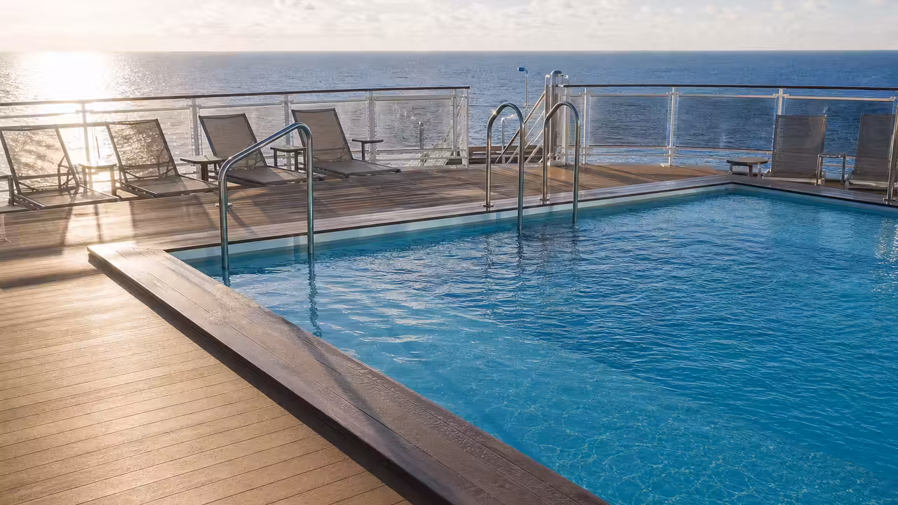 Piscine extérieure peu profonde sur le pont d’un navire de croisière, avec chaises longues face à la mer