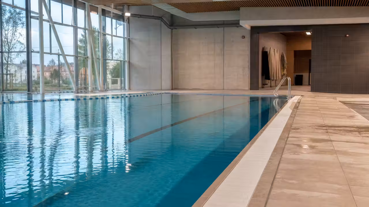 Bassin intérieur d’une piscine municipale avec lignes d’eau, vestiaires vitrés et lumière naturelle