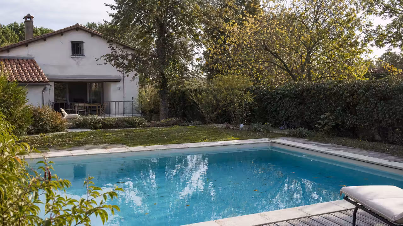 Piscine enterrée rectangulaire dans un jardin résidentiel, bordée d’une terrasse et d’une haie.