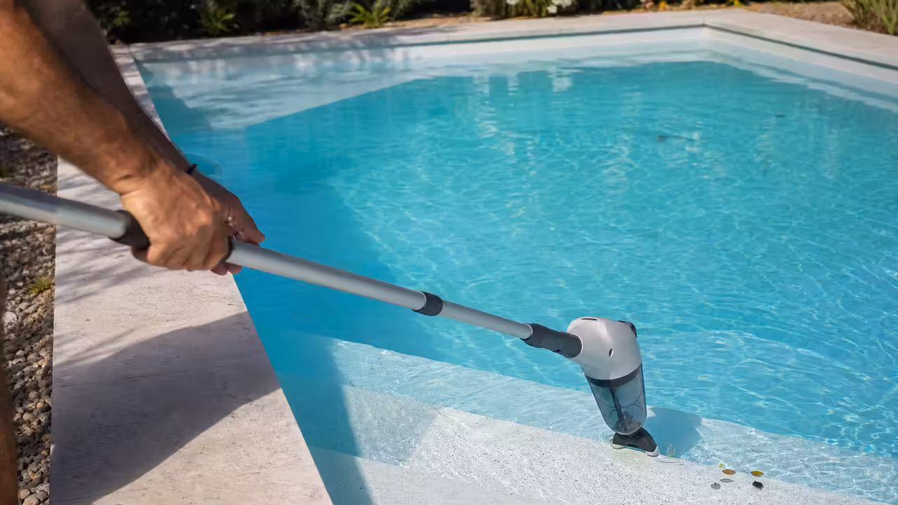 Aspirateur de piscine sans fil fixé à une perche au-dessus d’un petit bassin rectangulaire propre