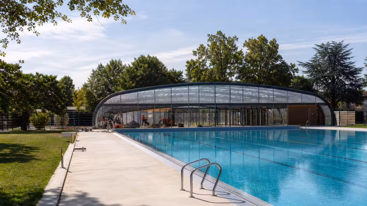 Vue d’ensemble d’une piscine municipale avec bassin extérieur et coupole rénovée dans un parc urbain