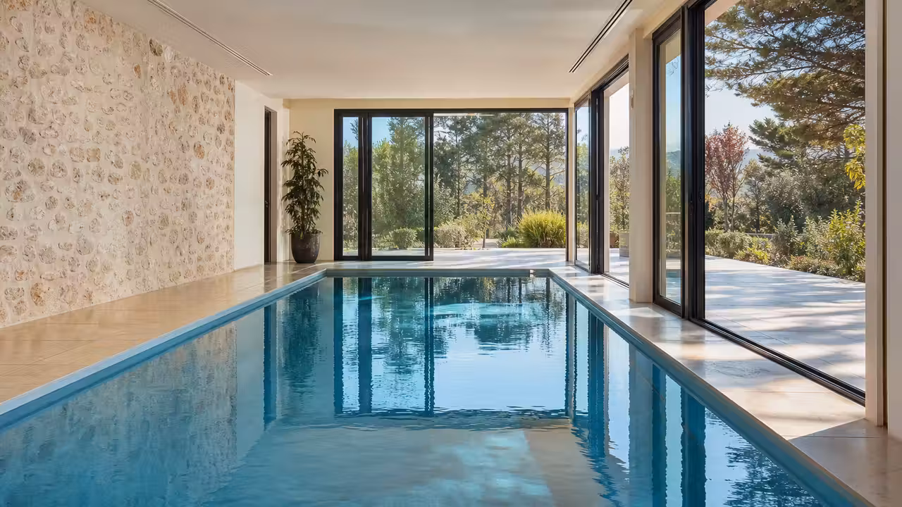 Bassin intérieur rectangulaire avec baies vitrées, plafond ventilé et plage en pierre claire
