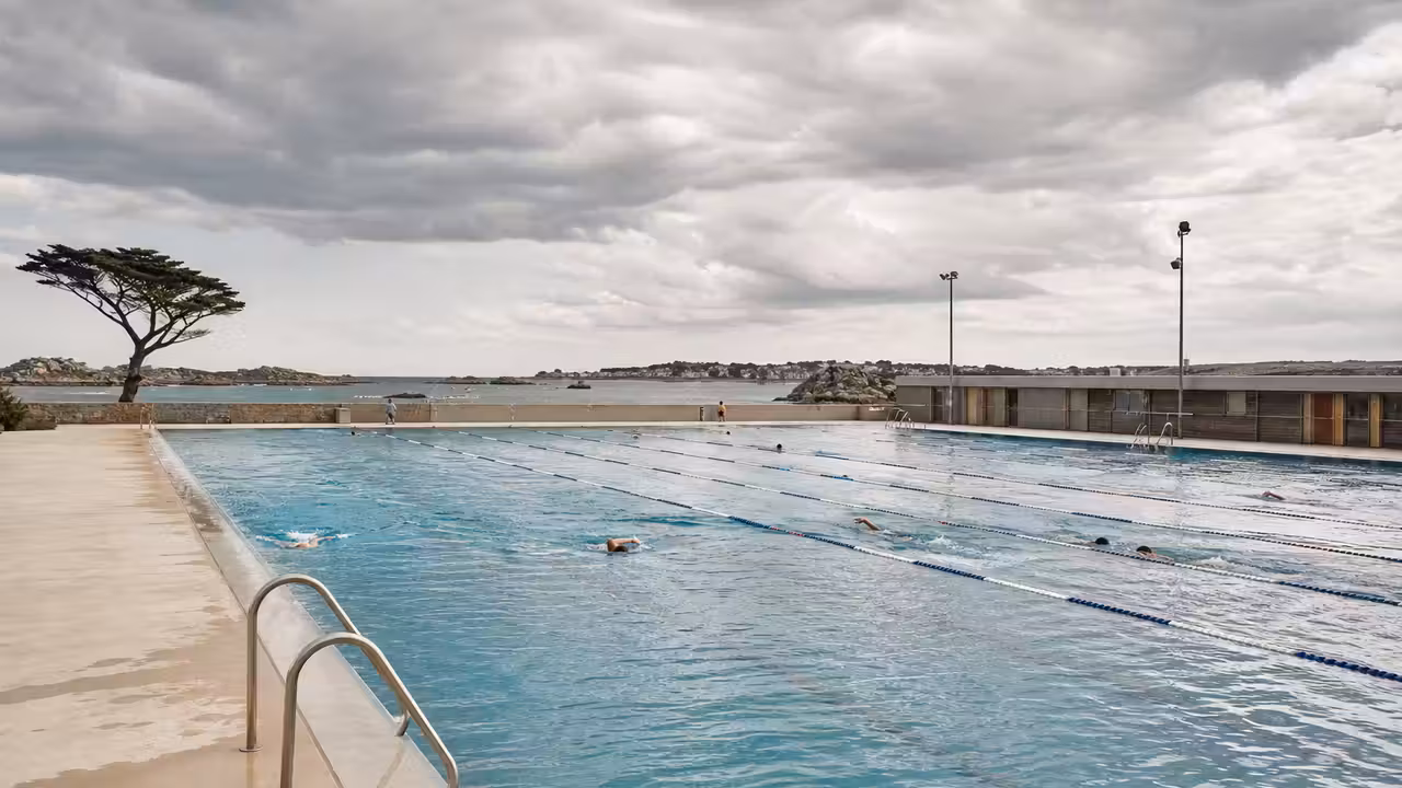 Bassin extérieur municipal de 50 mètres, lignes d’eau calmes et équipements discrets sous une lumière côtière