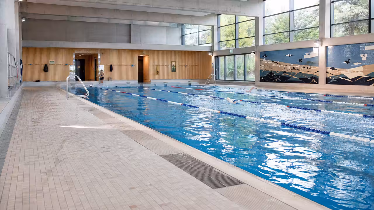 Bassin intérieur rénové d’une piscine publique avec lignes d’eau, baies vitrées et vestiaires modernisés