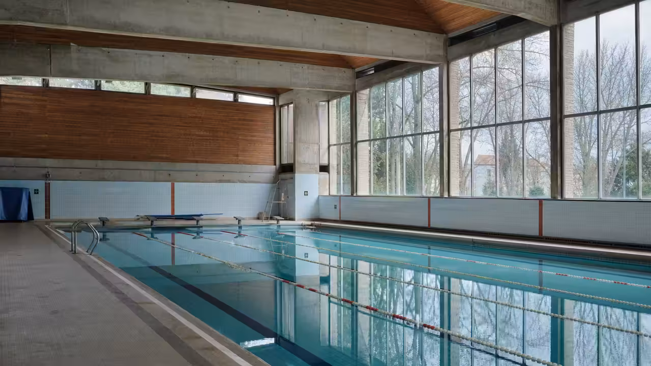 Intérieur d’une piscine municipale couverte ancienne, avec bassin, lignes d’eau et lumière naturelle
