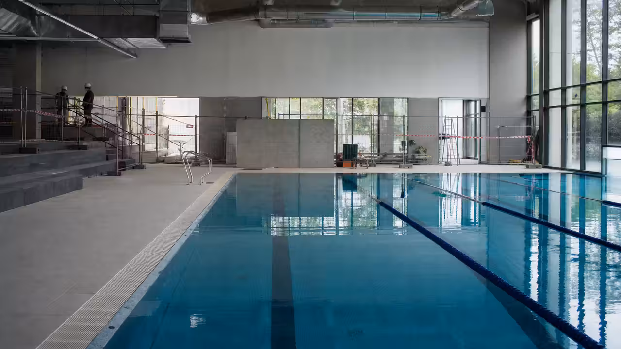 Bassin public à lignes d’eau dans un centre aquatique rénové, éclairé par une vaste baie vitrée