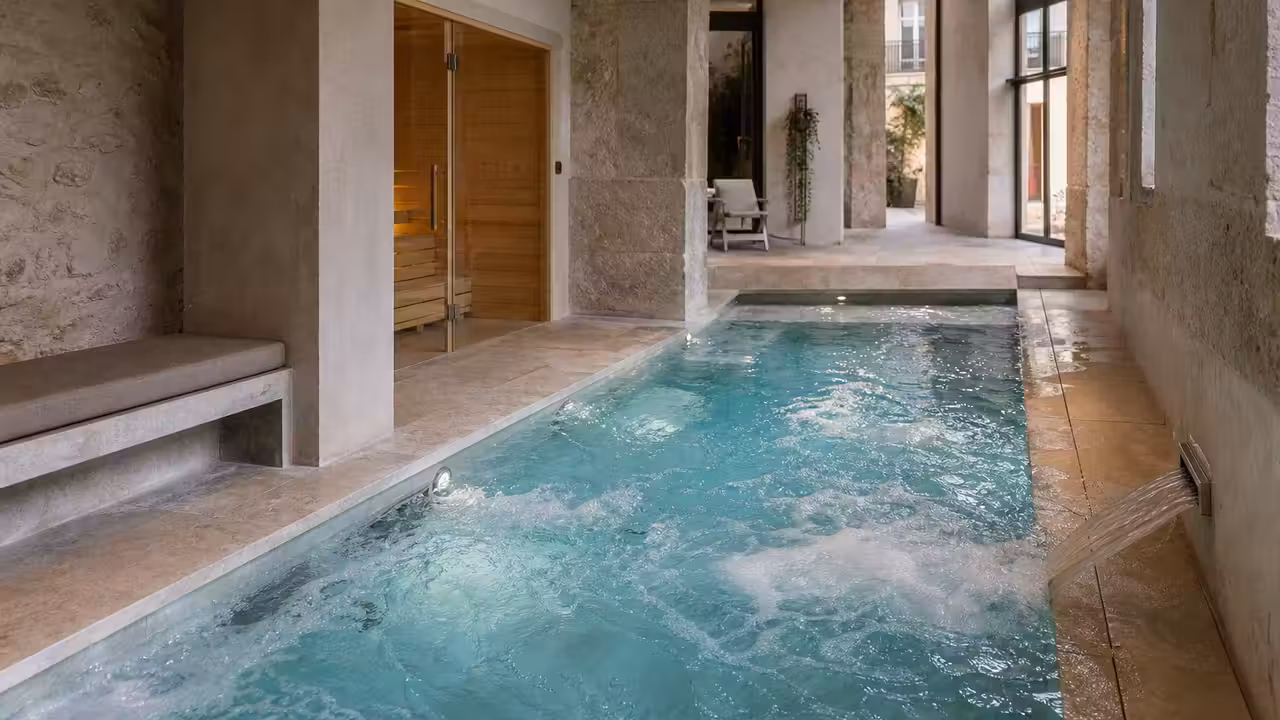 Espace bien-être d’hôtel avec petit bassin intérieur, jets balnéo, sauna vitré et lumière naturelle douce
