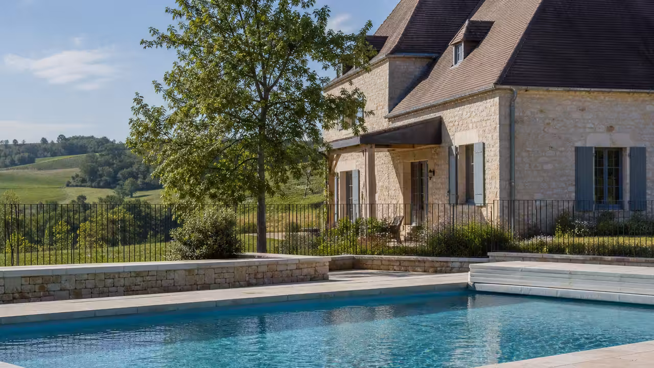 Piscine rectangulaire chauffée devant un gîte en pierre, avec terrasse sécurisée et paysage rural en arrière-plan