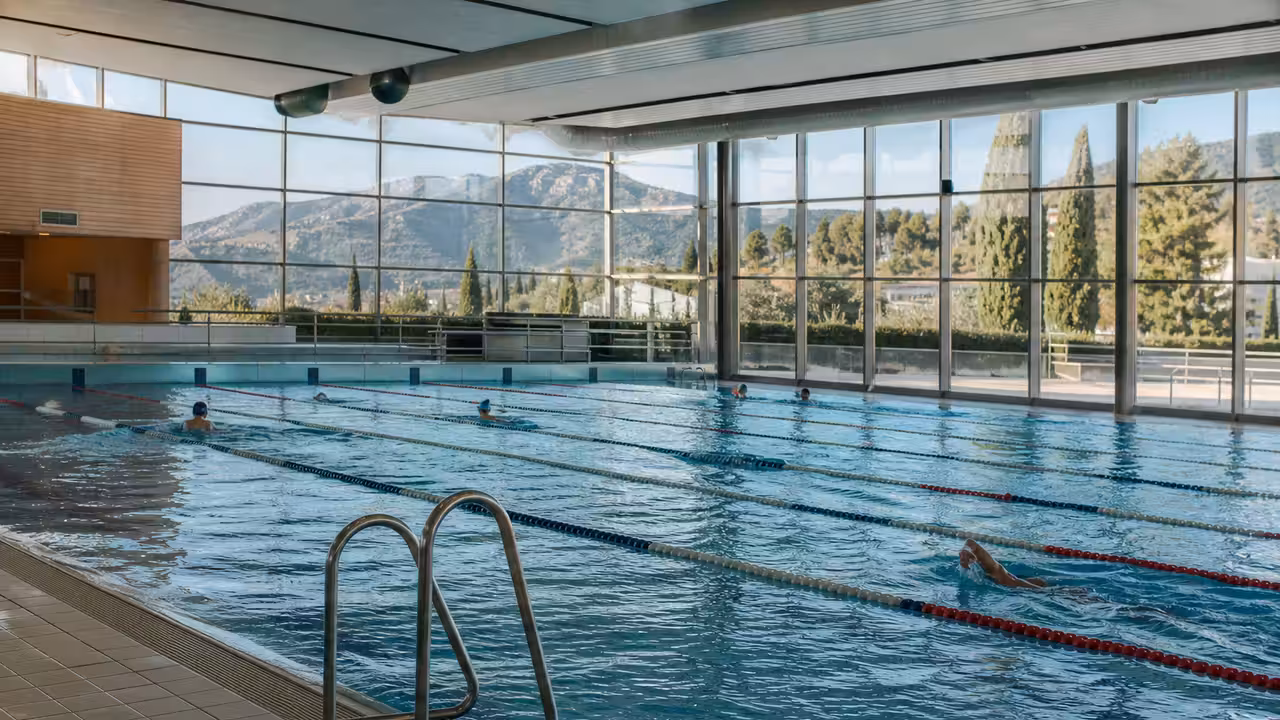 Bassin intérieur lumineux d’un centre aquatique public avec lignes de nage et larges baies vitrées