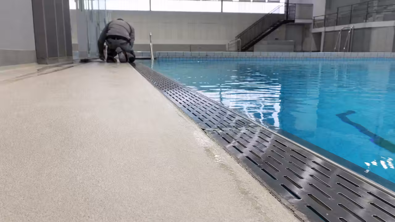 Plage en résine d’une piscine publique avec goulotte d’évacuation au bord d’un bassin intérieur