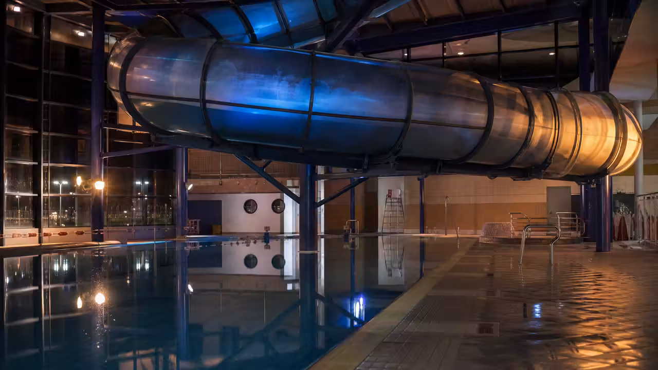Toboggan couvert d’une piscine publique éclairé de couleurs douces, avec bassin surveillé en arrière-plan