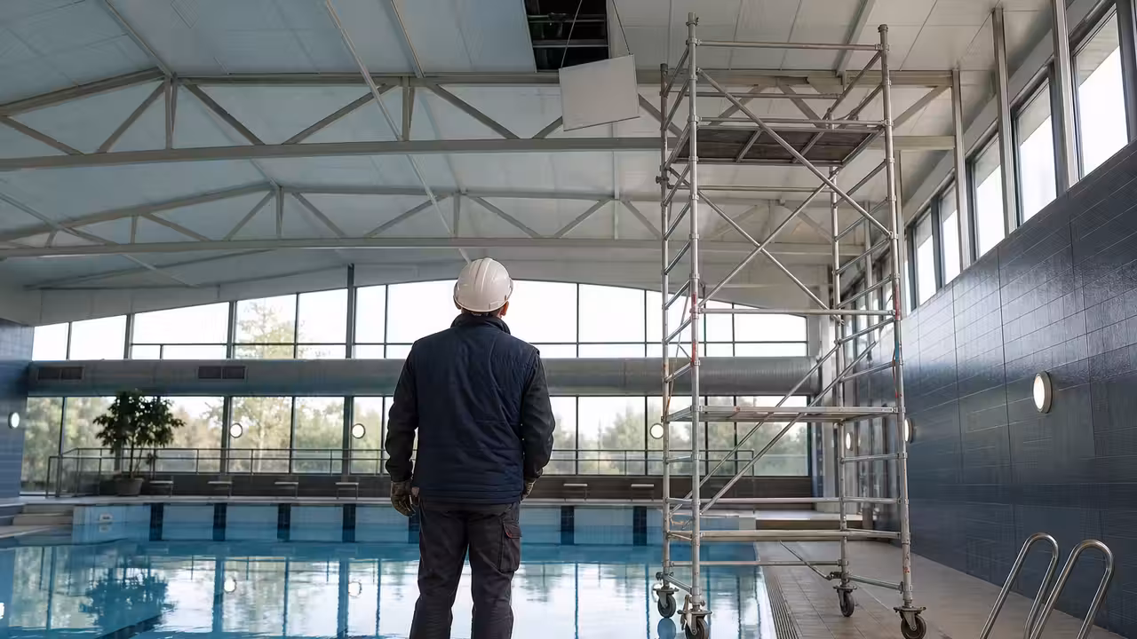 Toiture d’une piscine municipale couverte inspectée après des infiltrations d’eau, bassins vides au second plan