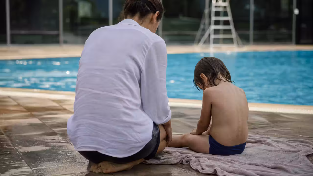 Parent observant prudemment un jeune enfant assis au bord d’un bassin après une séance de baignade