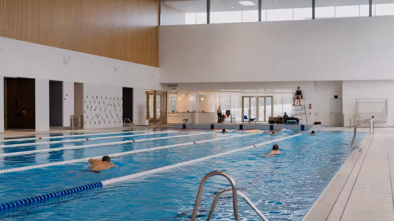 Nageurs dans un bassin municipal lumineux, avec couloirs de nage et accueil de piscine en arrière-plan
