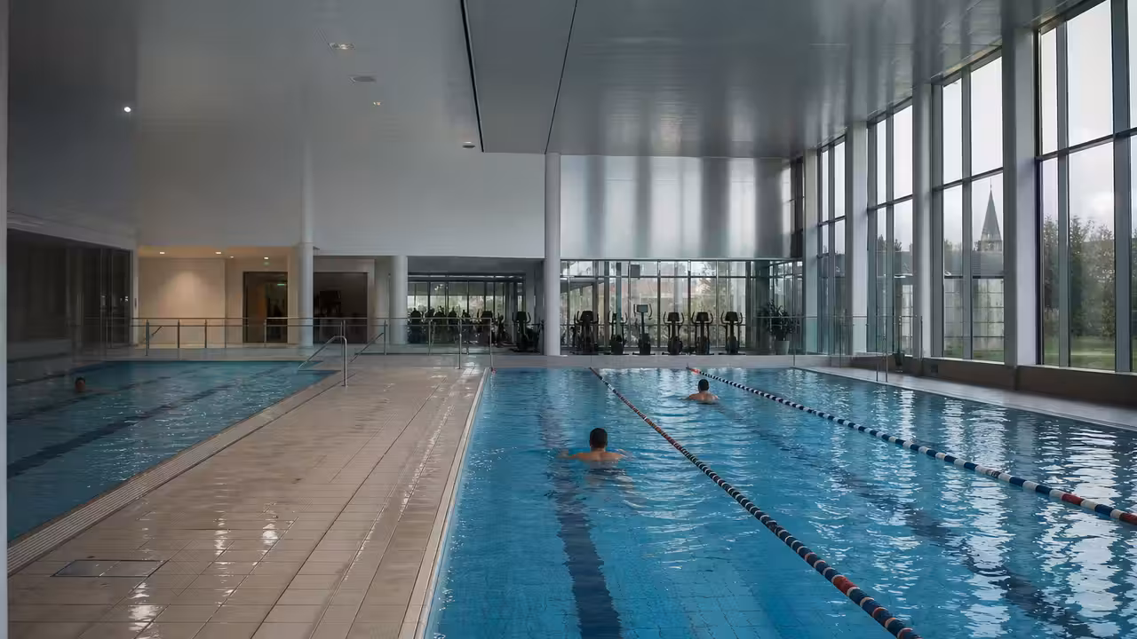 Vue intérieure d’un centre aquatique moderne avec bassin de nage, baies vitrées et espaces de détente