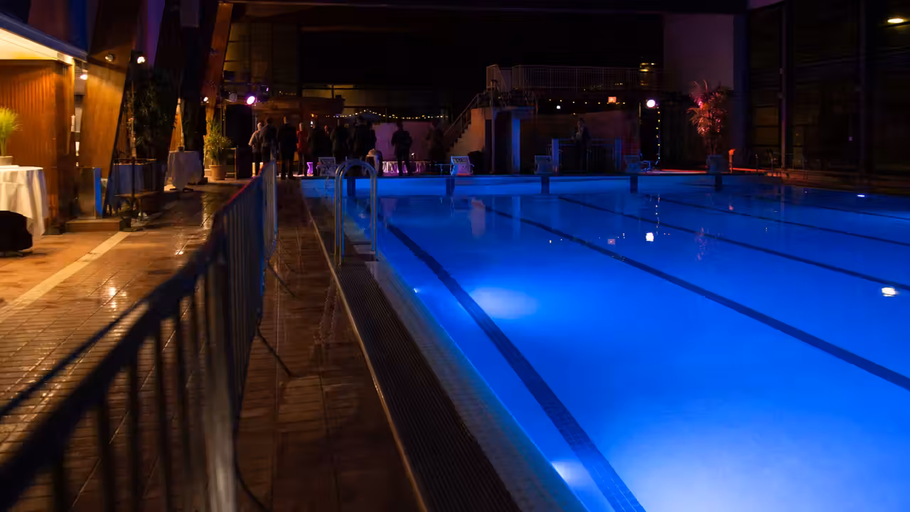 Ambiance nocturne dans une piscine municipale, avec éclairages colorés sur les bassins et plages sécurisées