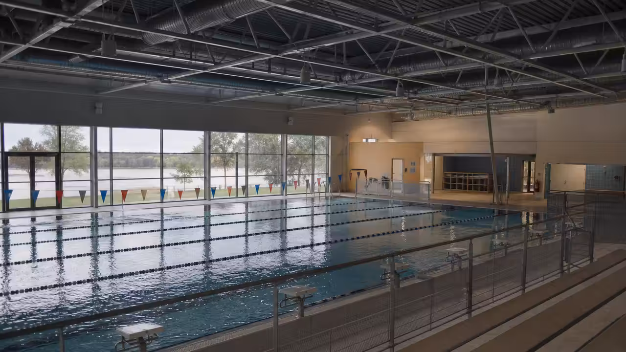 Bassin sportif couvert d’une piscine municipale, lignes d’eau calmes et grandes baies vitrées en lumière naturelle