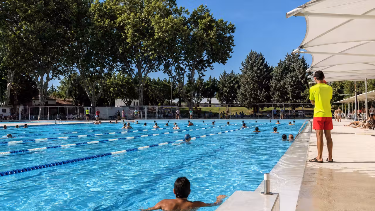 Bassin extérieur municipal très fréquenté durant une chaude journée d’été, avec surveillant au bord de l’eau