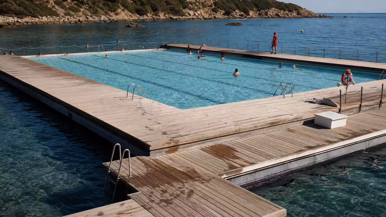 Bassin flottant rectangulaire avec couloirs de nage, ponton en bois et mer calme sur le littoral corse
