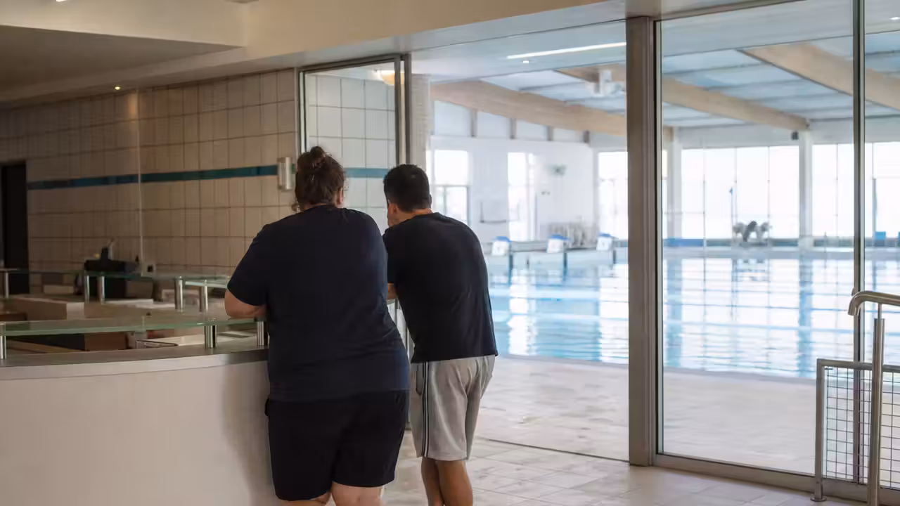 Entrée d’une piscine municipale avec bassin couvert et agent d’accueil en arrière-plan, sans visage identifiable