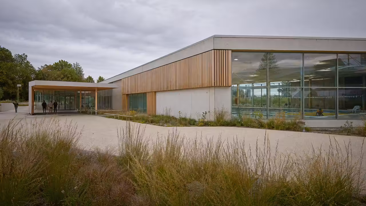 Vue intérieure d’un bassin sportif couvert de 50 mètres en chantier, avec charpente et lumière naturelle