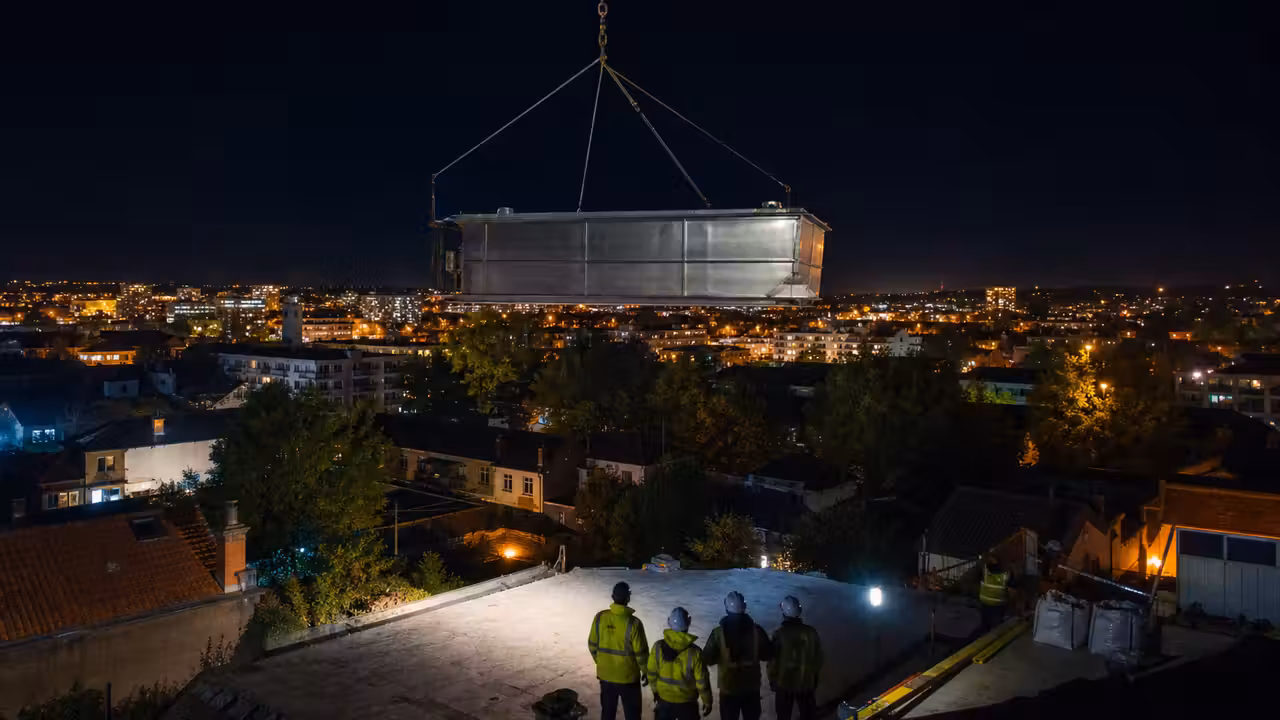Piscine en acier inoxydable suspendue à un câble lors d’une livraison nocturne en milieu urbain