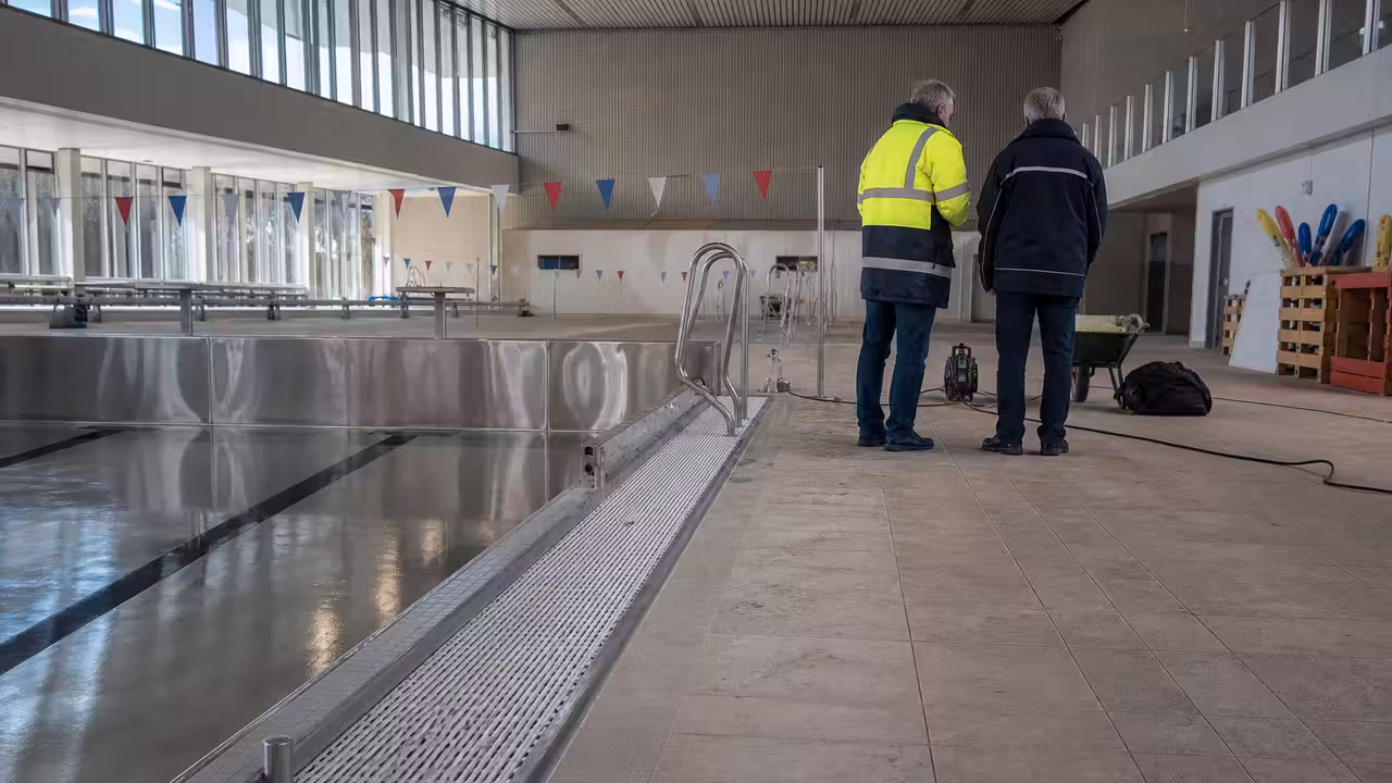 Bassin public en acier inoxydable vide, avec lignes d’eau et goulotte visibles pendant une inspection technique