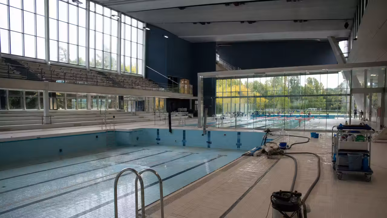 Bassin sportif intérieur vide pendant une fermeture technique, avec gradins et grandes baies vitrées