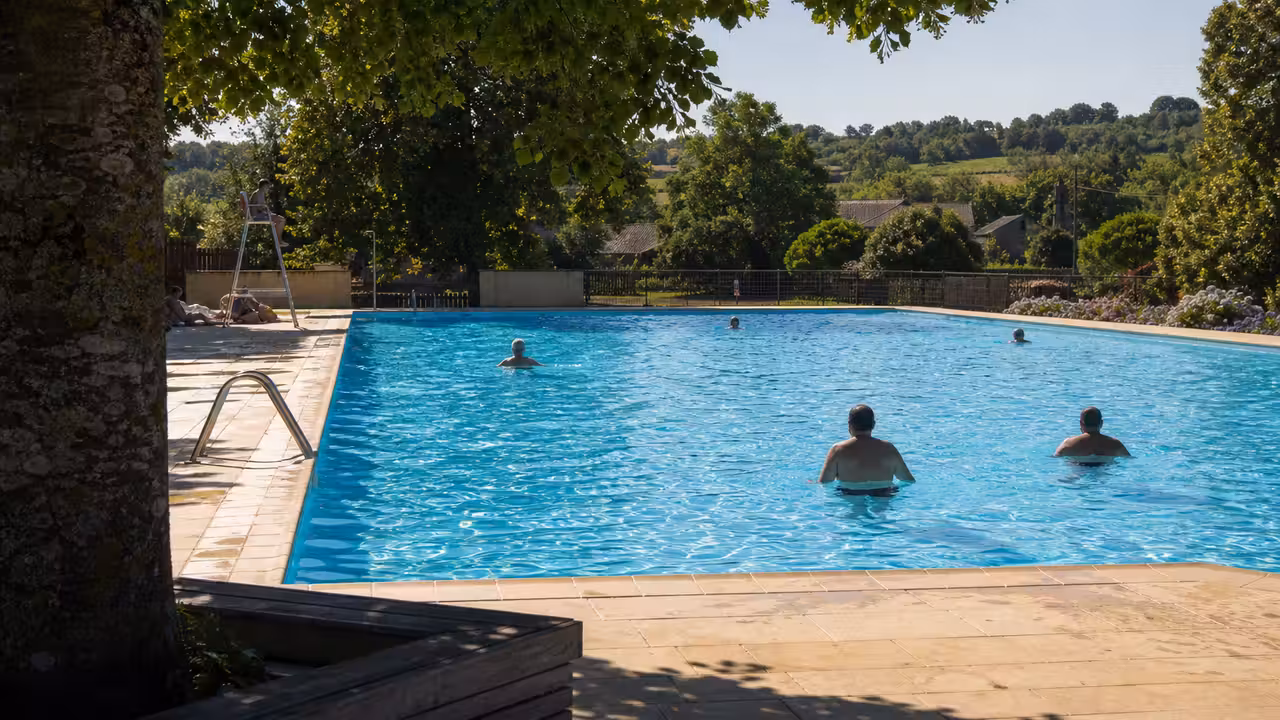 Bassin extérieur municipal entouré de verdure, avec nageurs et zone de détente lors d’une chaude journée d’été