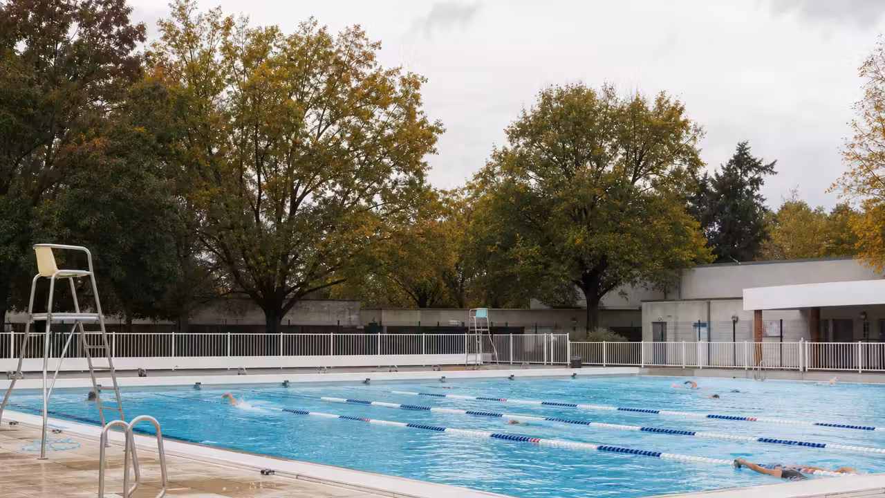 Bassin extérieur municipal calme en automne, avec lignes d’eau et arbres aux couleurs de fin de saison