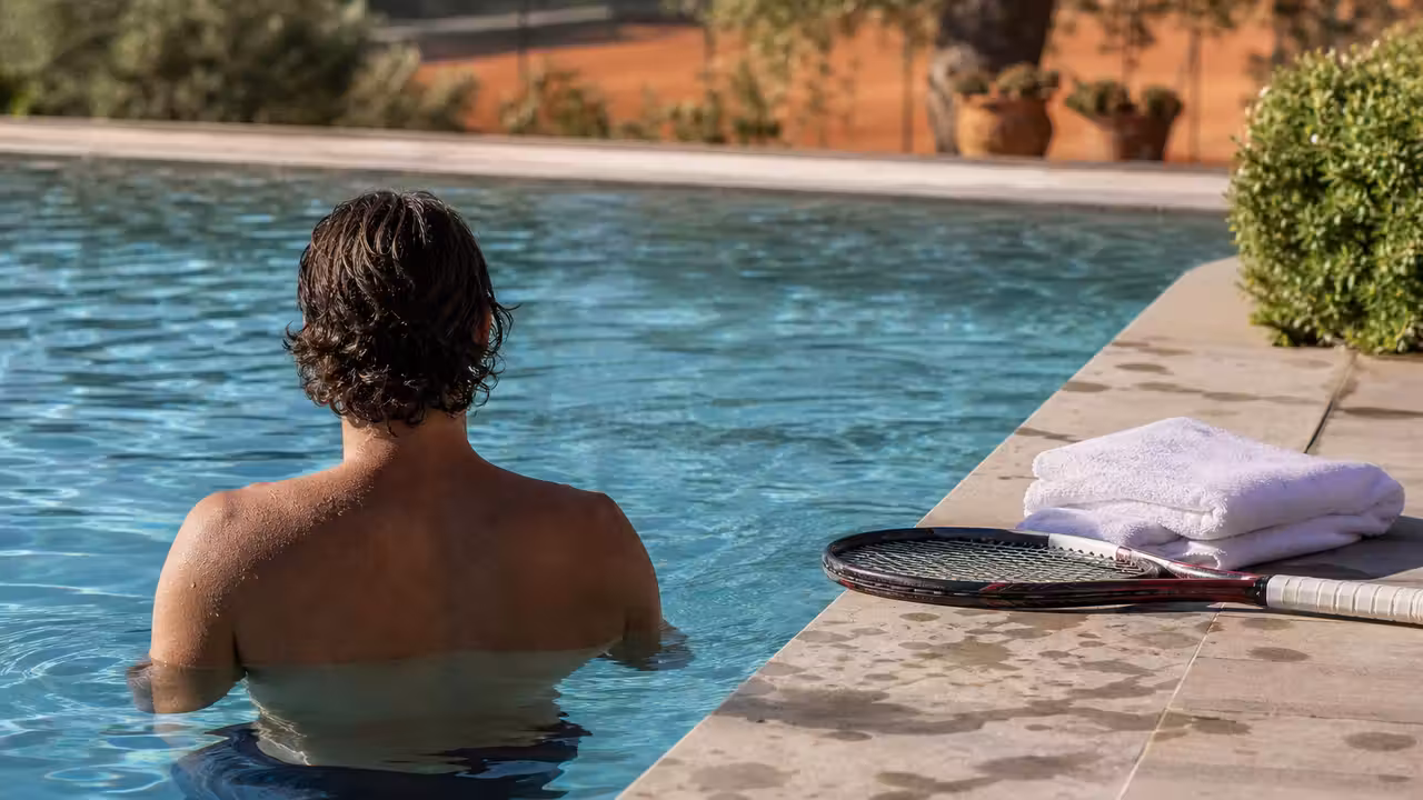 Joueur de tennis se détendant dans une piscine après l’entraînement, avec matériel sportif posé au bord