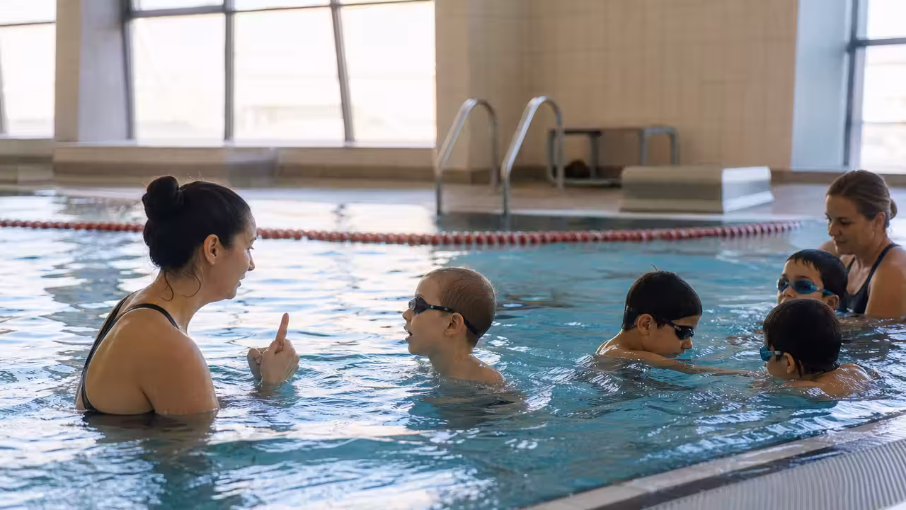 Enfants accompagnés par des éducateurs lors d’une séance de natation adaptée dans un bassin couvert.