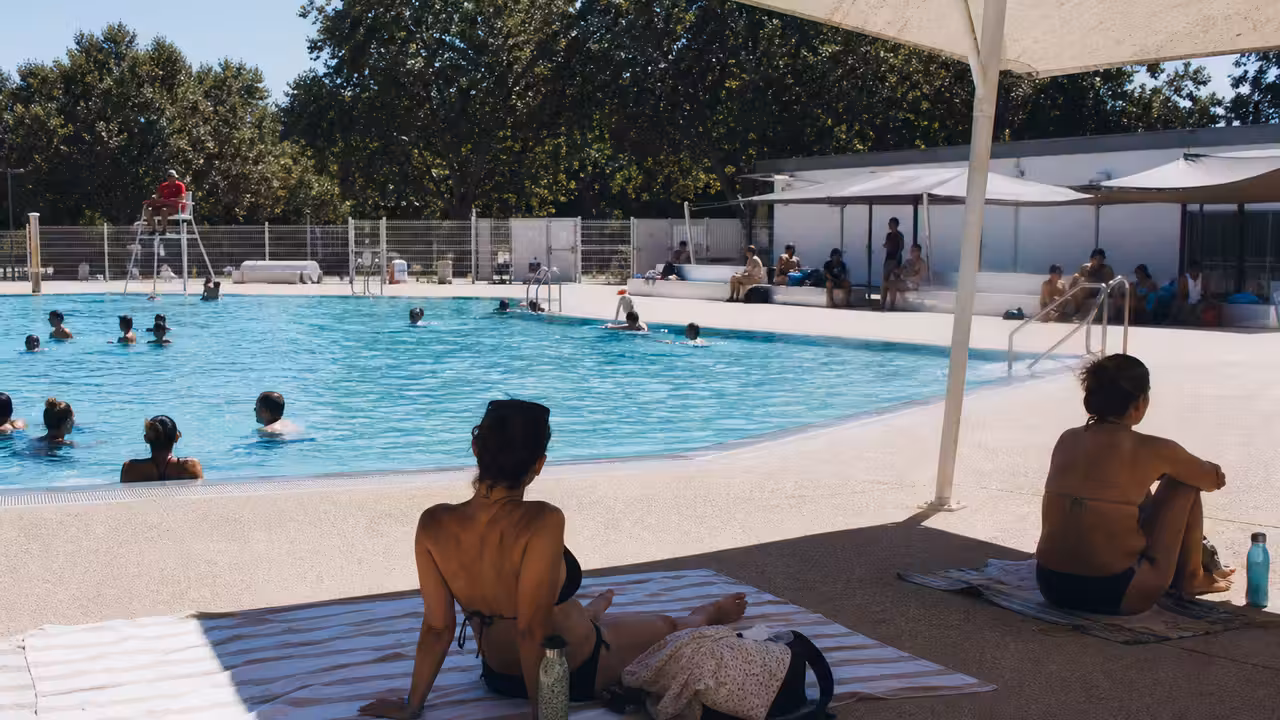 Bassin extérieur d’une piscine municipale fréquentée en été, avec zones d’ombre et surveillance des baigneurs