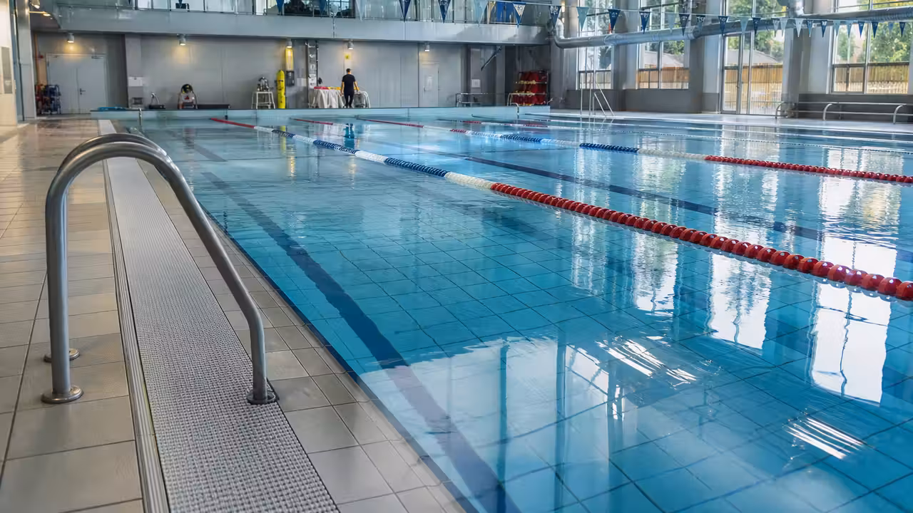 Bassin intérieur d’une piscine municipale rénovée, avec lignes d’eau et installations techniques en arrière-plan