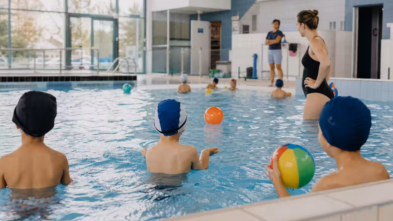 Enfants encadrés lors d’un atelier aquatique avec ballons dans une piscine municipale lumineuse