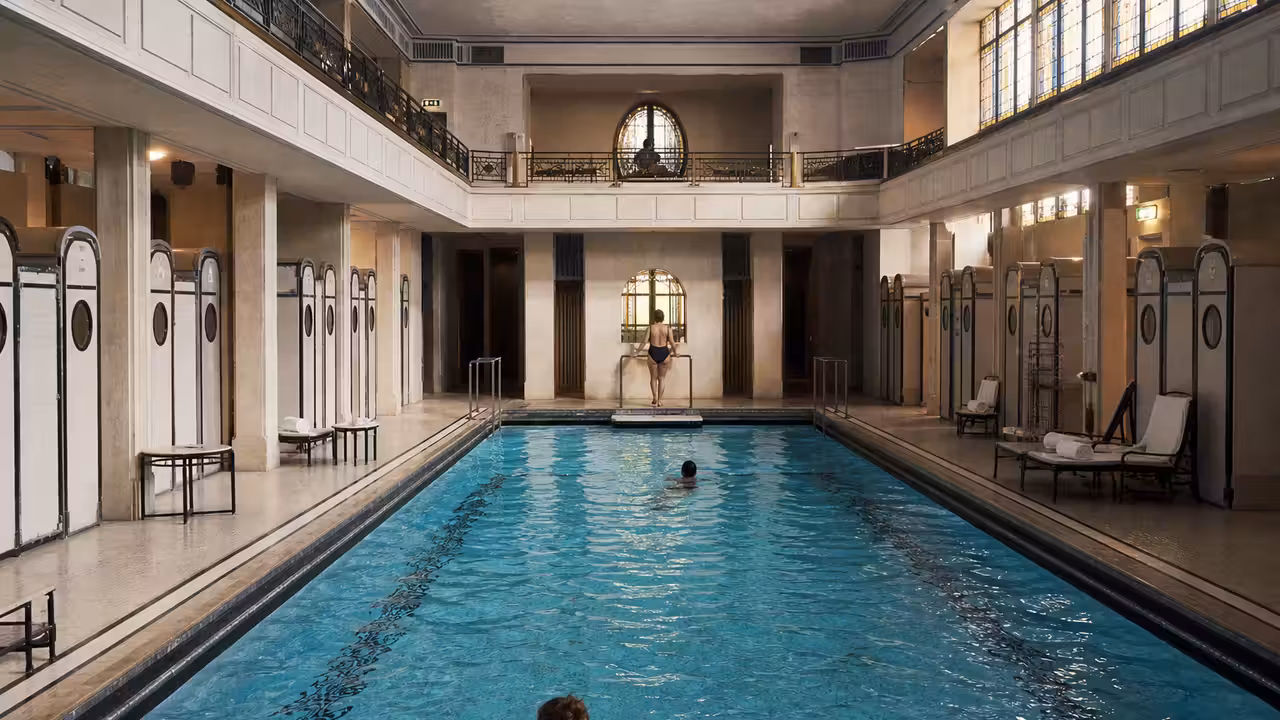 Bassin Art déco d’un hôtel parisien, bordé de cabines et baigné d’une lumière estivale douce