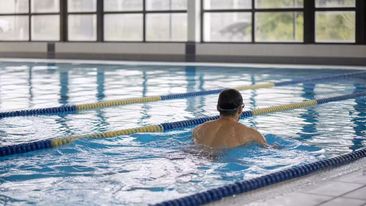 Ligne d’eau d’une piscine intérieure avec une nageuse équipée de lunettes, vue de dos