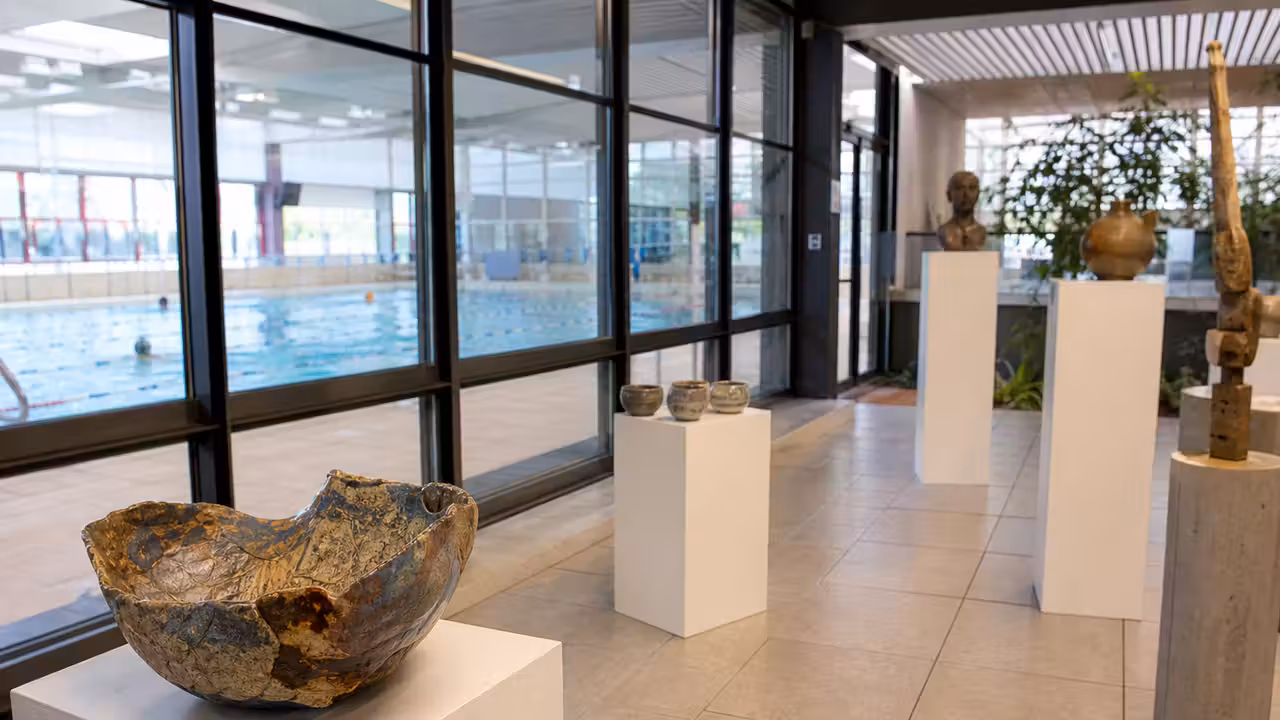 Exposition d’œuvres artisanales dans le hall lumineux d’une piscine municipale, près des baies vitrées